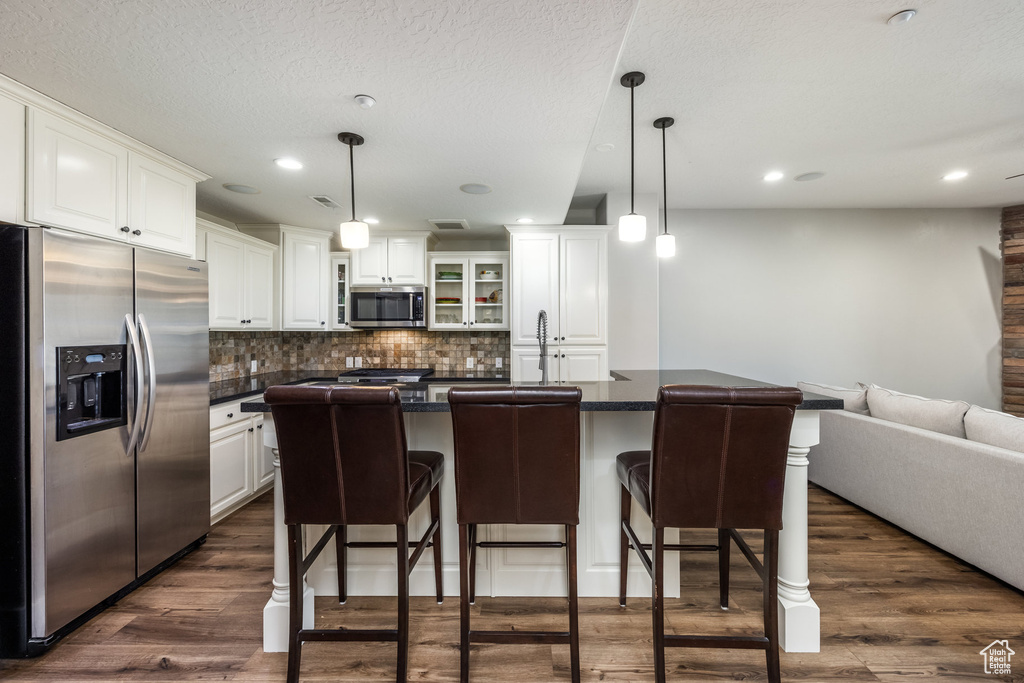 Kitchen with stainless steel appliances, dark countertops, white cabinets, backsplash, and a breakfast bar area