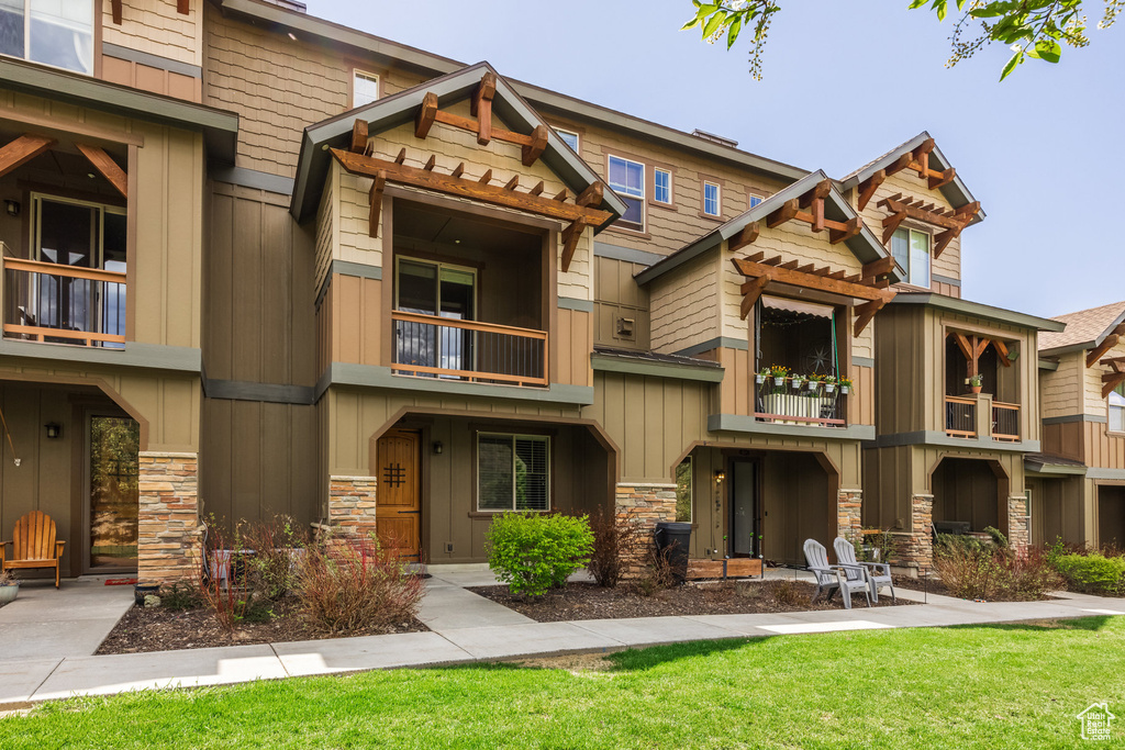 View of front of property featuring a balcony, stone siding, a front lawn, and board and batten siding