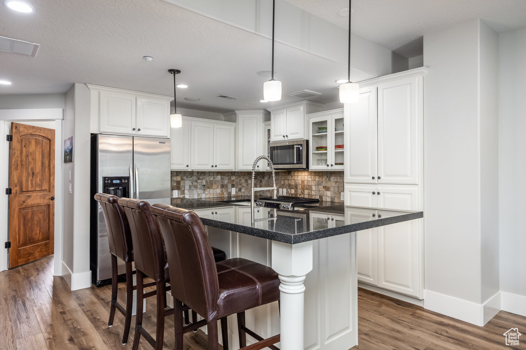 Kitchen with stainless steel appliances, dark wood-style floors, backsplash, white cabinetry, and a breakfast bar