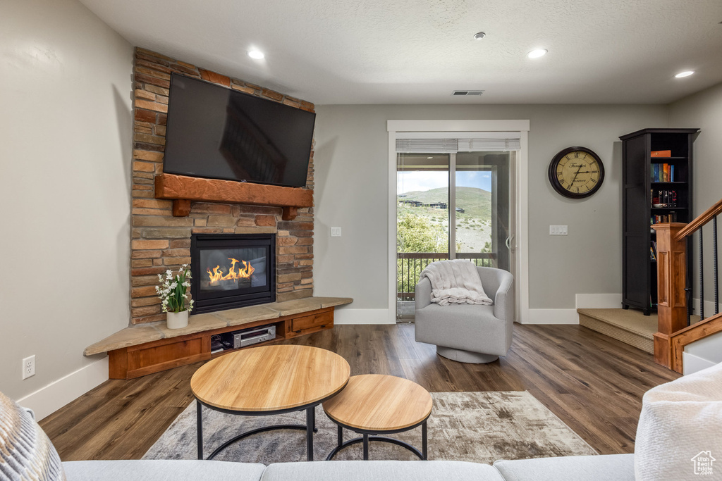 Living area with a stone fireplace, wood finished floors, recessed lighting, and stairway