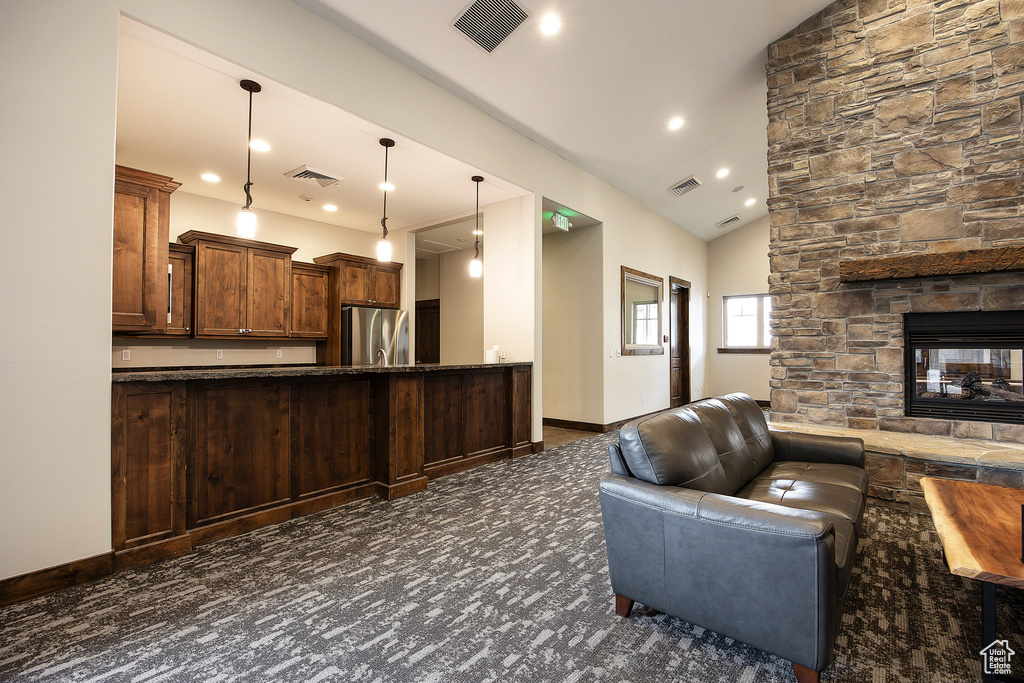 Kitchen featuring stainless steel fridge, open floor plan, vaulted ceiling, a stone fireplace, and recessed lighting