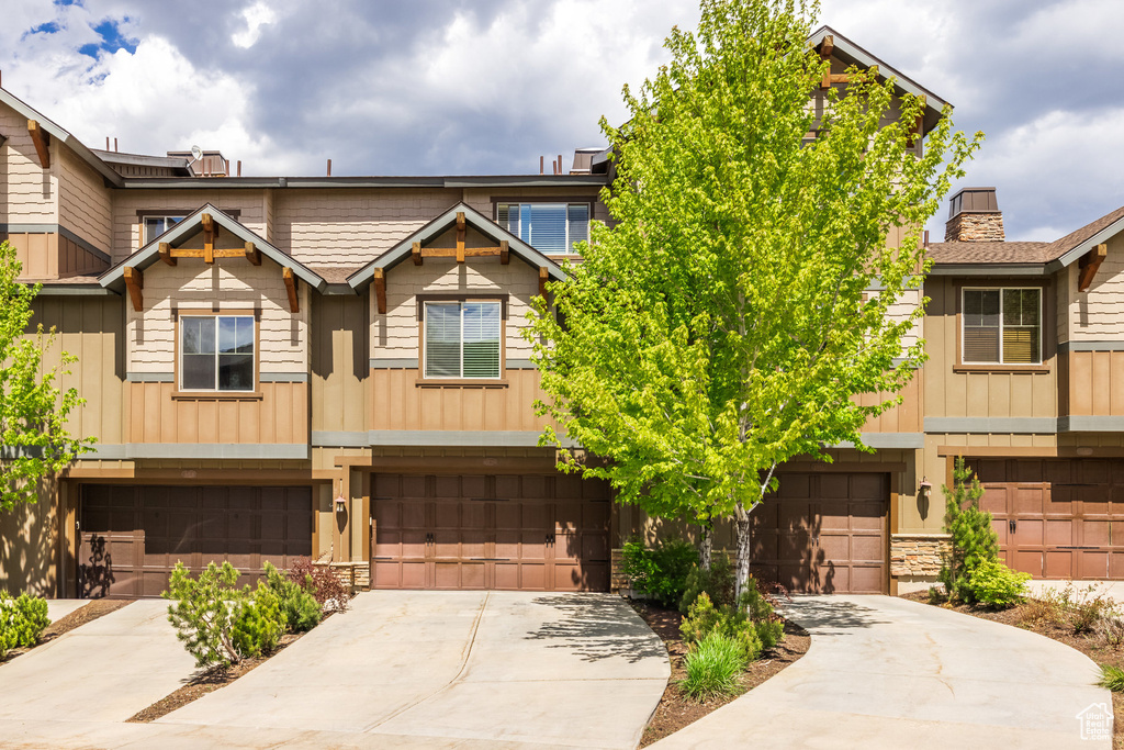 Townhome / multi-family property with driveway, board and batten siding, an attached garage, and a chimney