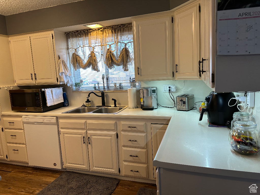 Kitchen with stainless steel microwave, light countertops, dishwasher, a sink, and white cabinetry