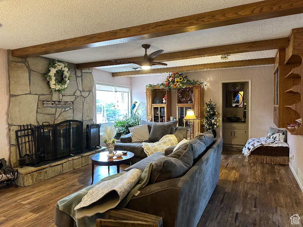Living area featuring wood finished floors, a fireplace, beam ceiling, a ceiling fan, and a textured ceiling