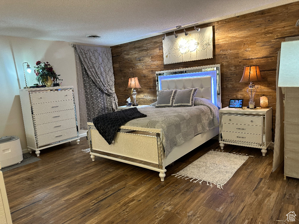 Bedroom with a textured ceiling, wood walls, and wood finished floors