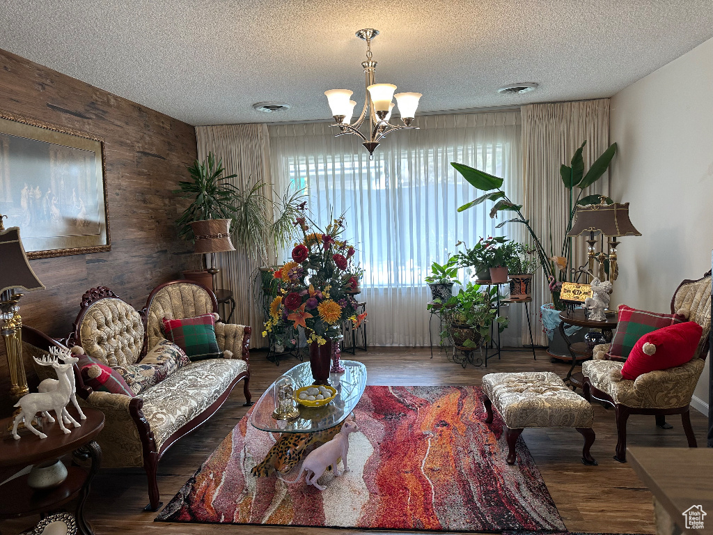 Living area featuring a chandelier, visible vents, wood walls, a textured ceiling, and wood finished floors