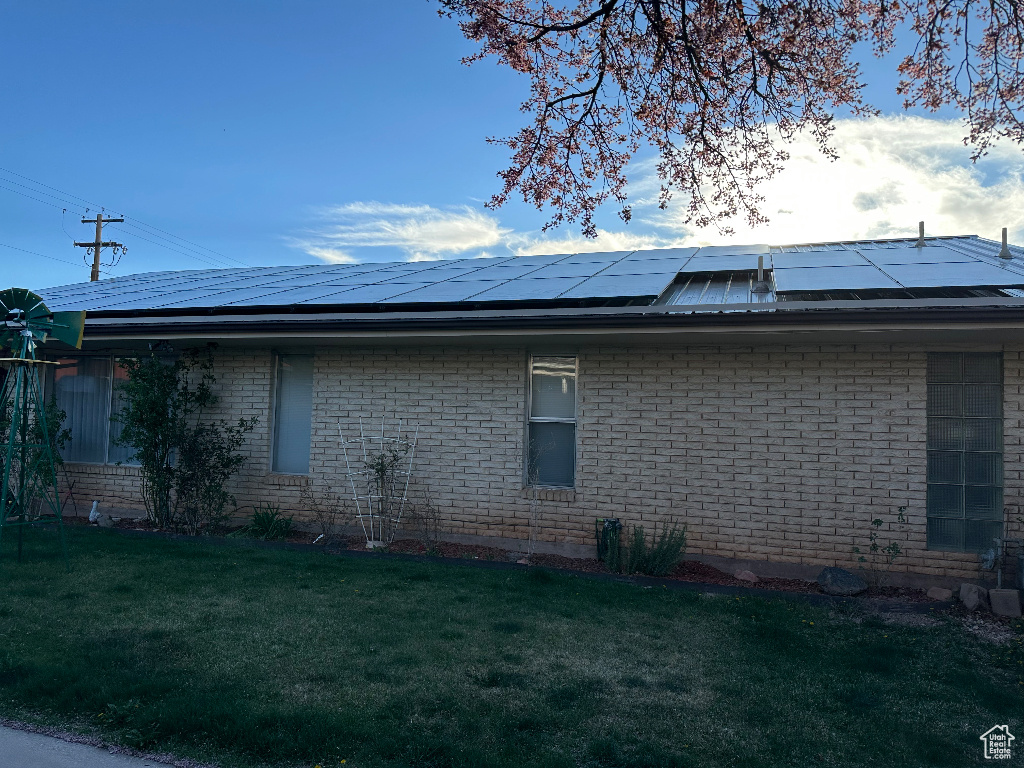View of property exterior featuring solar panels, a yard, and brick siding