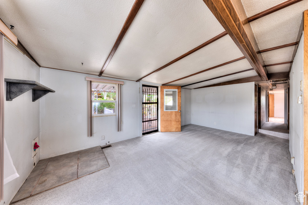 Unfurnished living room with a textured ceiling, carpet, and beam ceiling