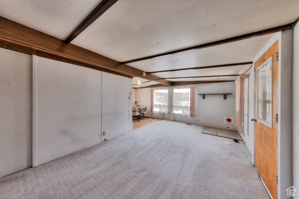 Unfurnished living room featuring vaulted ceiling with beams, carpet, and a textured ceiling