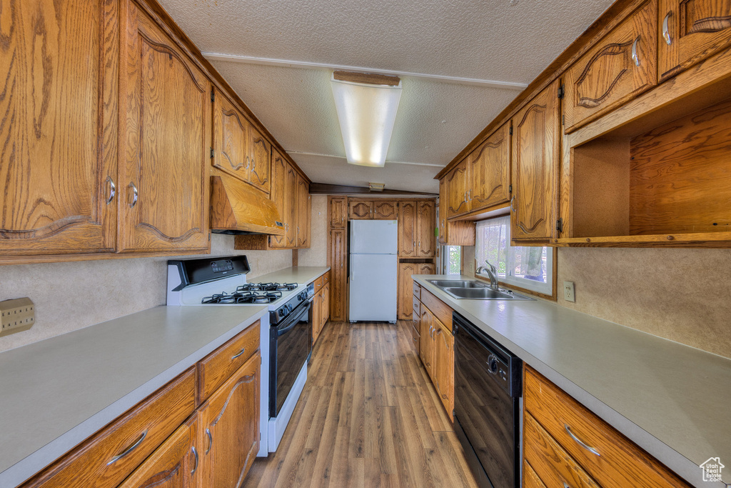 Kitchen with freestanding refrigerator, custom exhaust hood, black dishwasher, a sink, and gas stove