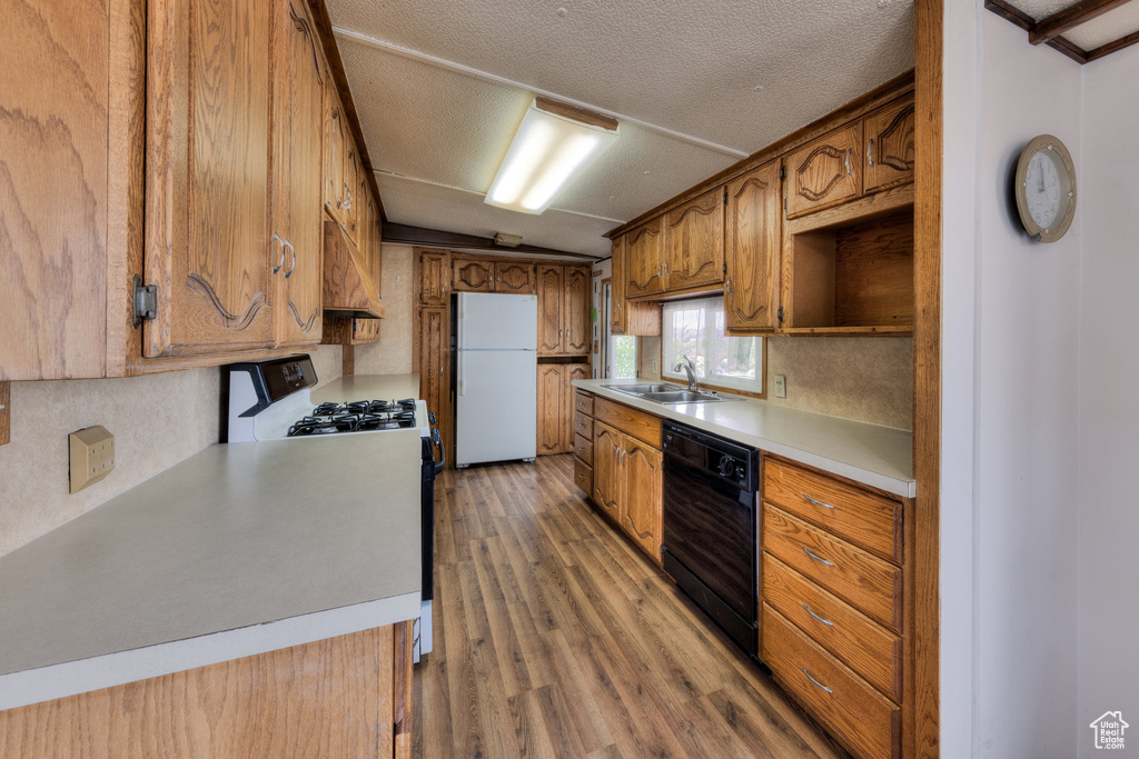 Kitchen with gas stove, dishwasher, freestanding refrigerator, lofted ceiling, and light wood-type flooring