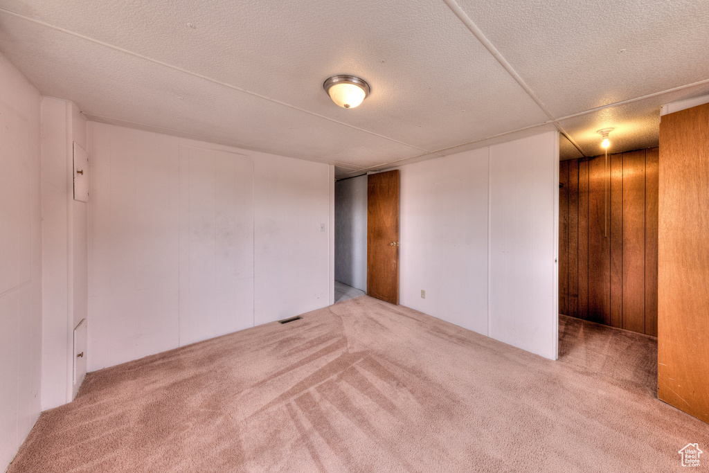 Empty room with visible vents, carpet flooring, a textured ceiling, and wooden walls