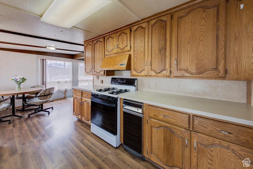 Kitchen featuring under cabinet range hood, brown cabinets, gas range oven, and light countertops