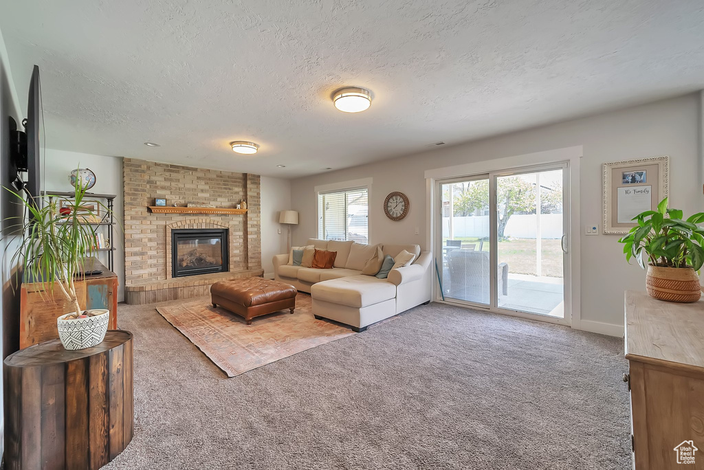 Carpeted living room with a textured ceiling, baseboards, and a brick fireplace
