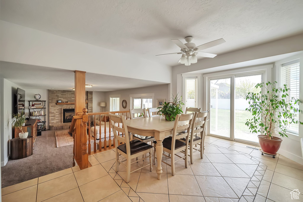 Dining room featuring light tile patterned floors, ceiling fan, baseboards, and a brick fireplace
