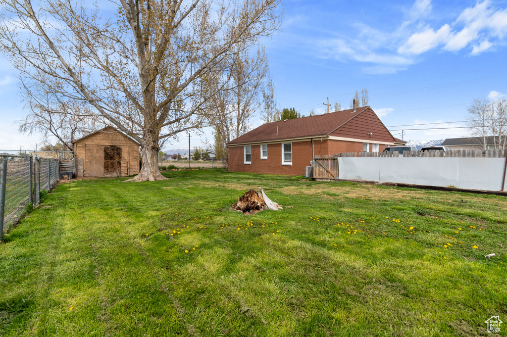 View of yard featuring central AC, a fenced backyard, an outbuilding, an outdoor fire pit, and a storage shed