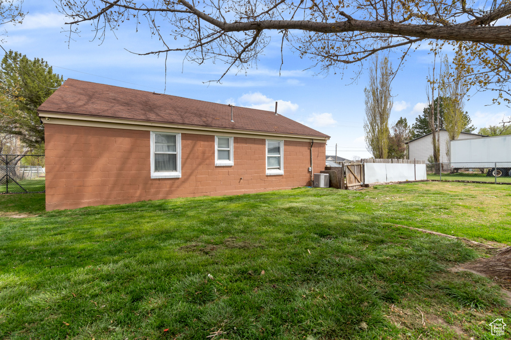 Back of property with concrete block siding, roof with shingles, fence, and a yard
