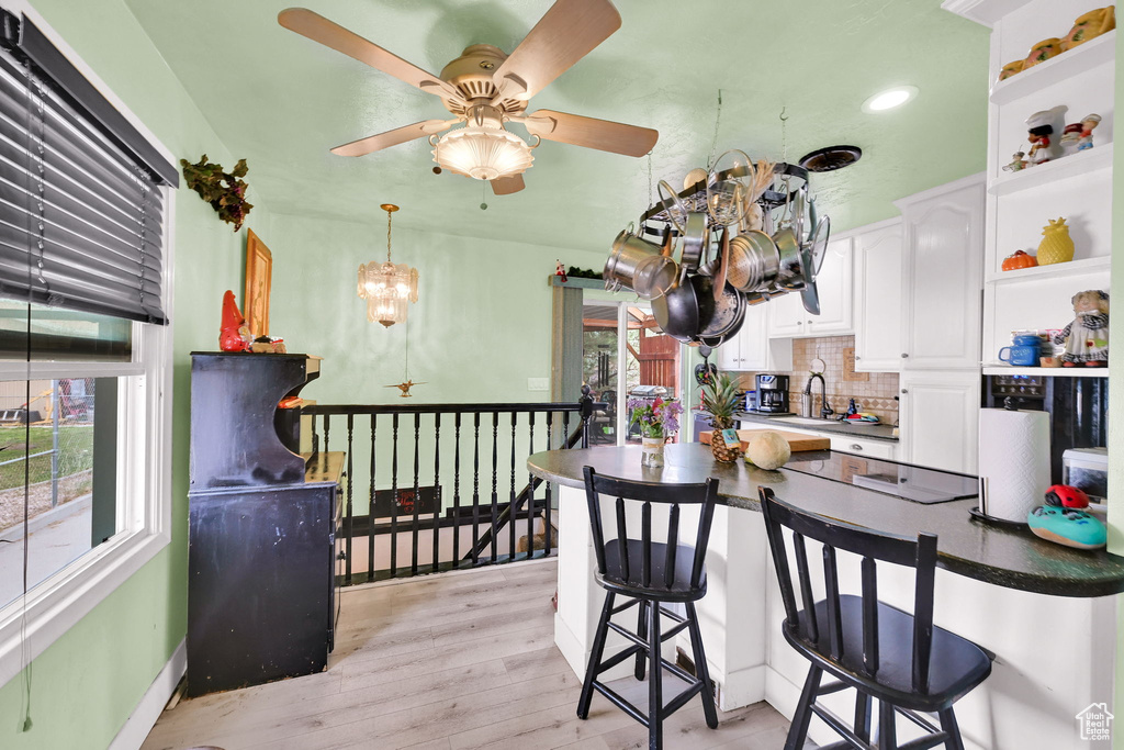 Kitchen with tasteful backsplash, a breakfast bar, light wood finished floors, white cabinetry, and a peninsula