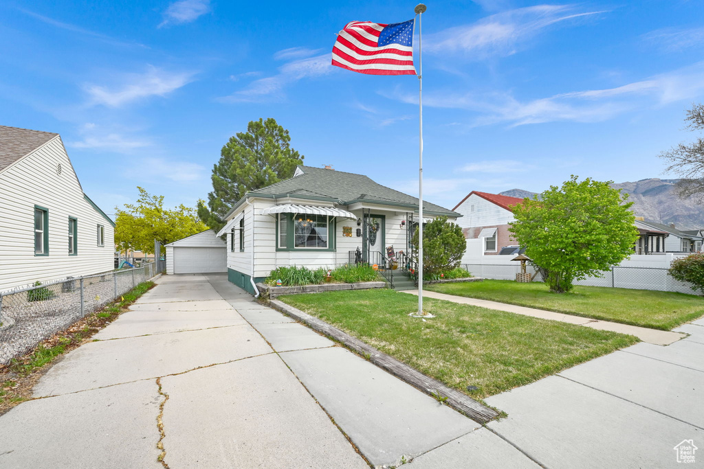 View of front of home with a front lawn, a garage, an outdoor structure, roof with shingles, and fence