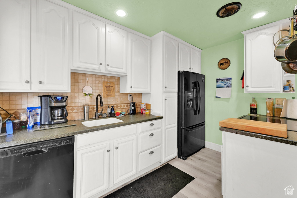 Kitchen with light wood-style flooring, white cabinets, black appliances, a sink, and baseboards