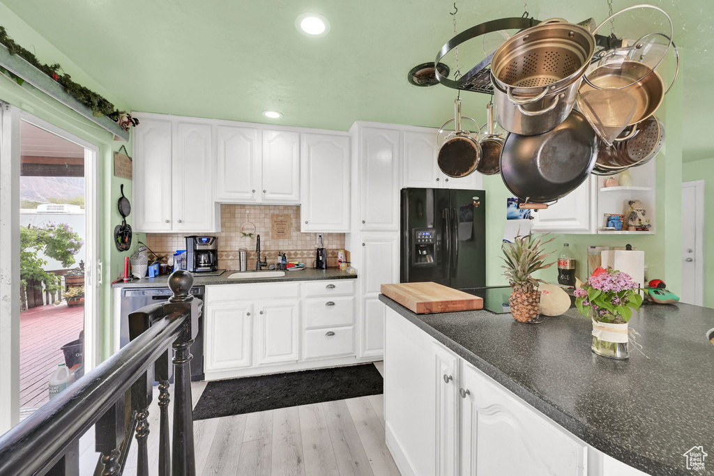 Kitchen with white cabinets, a sink, dark countertops, wood finished floors, and black fridge