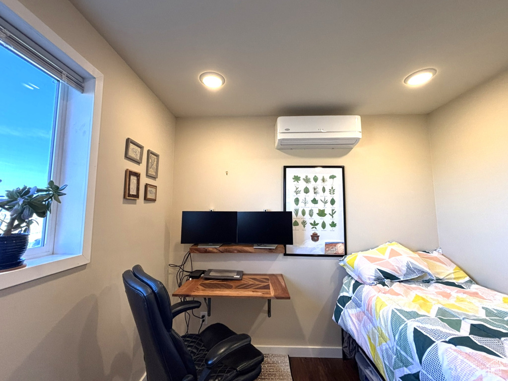 Bedroom with wood finished floors, a wall unit AC, recessed lighting, and baseboards