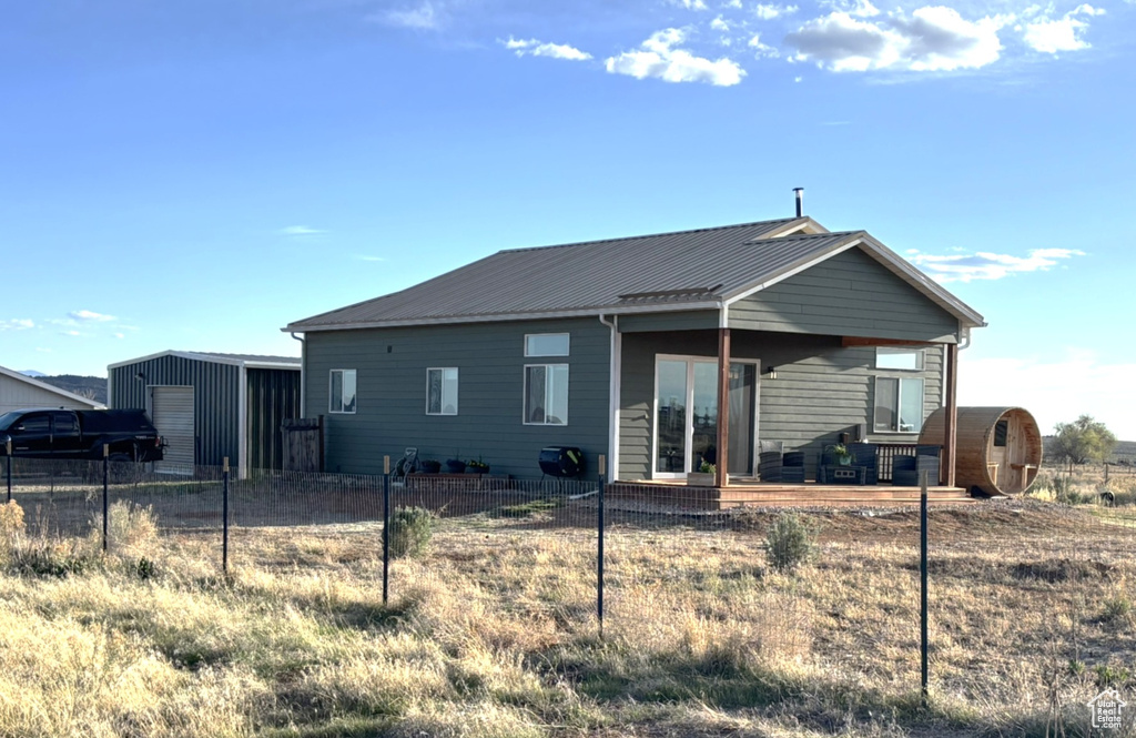 Back of property with fence, an outdoor structure, metal roof, and a wooden deck