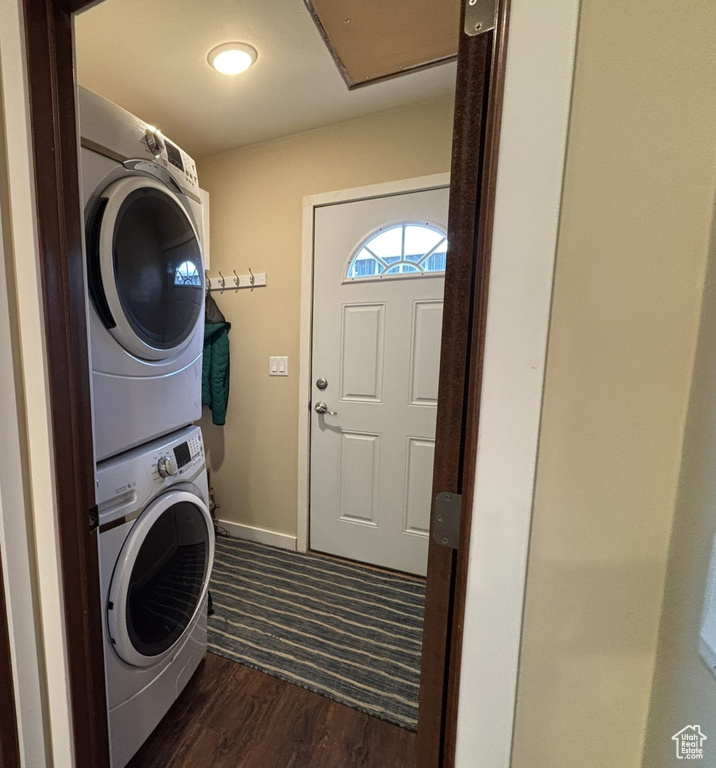 Clothes washing area featuring stacked washer and dryer, dark wood-style flooring, laundry area, and baseboards