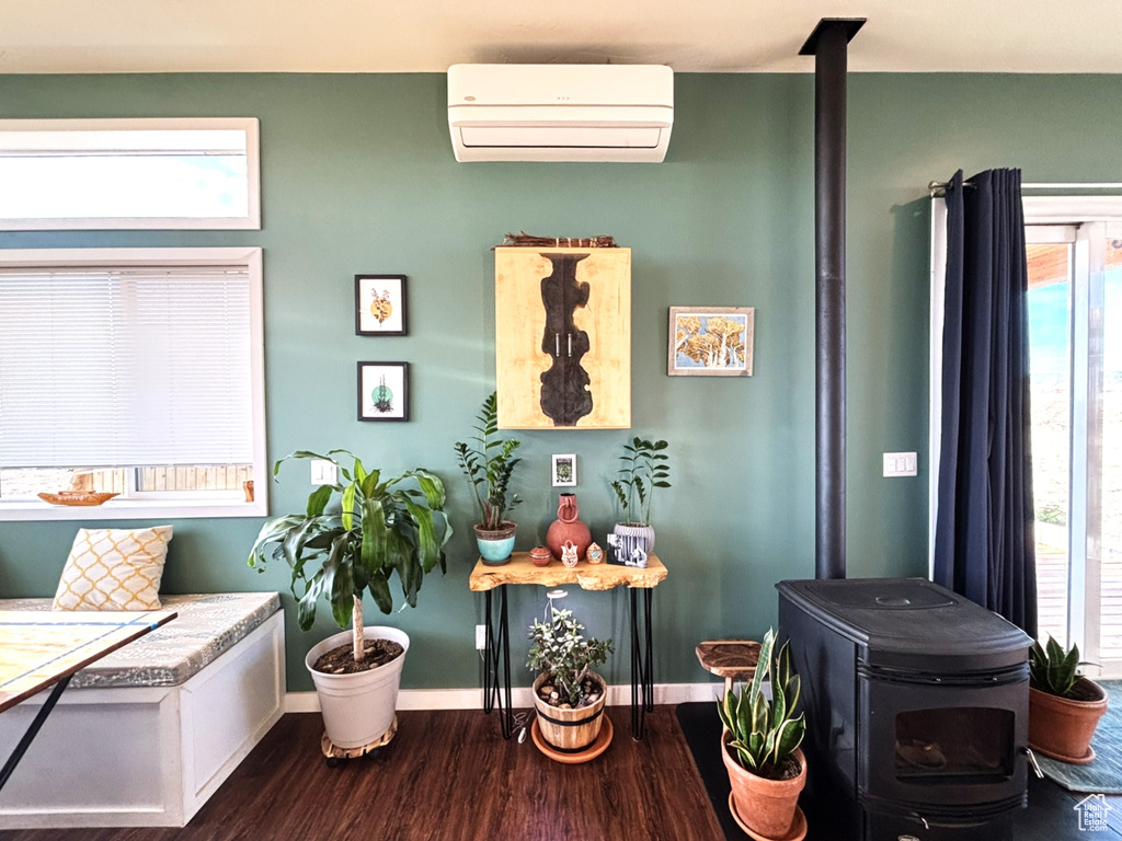 Interior space with wood finished floors, a wall mounted air conditioner, a wood stove, and baseboards