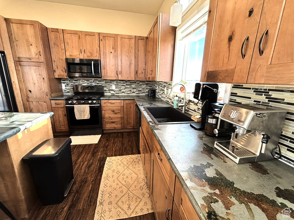 Kitchen featuring brown cabinetry, black appliances, backsplash, a sink, and dark wood-type flooring