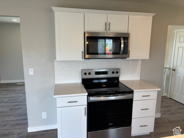 Kitchen featuring stainless steel appliances, decorative backsplash, dark wood finished floors, and baseboards
