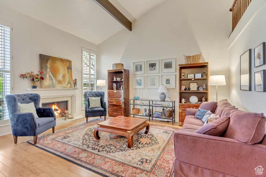 Living room featuring beamed ceiling, a premium fireplace, wood finished floors, and high vaulted ceiling