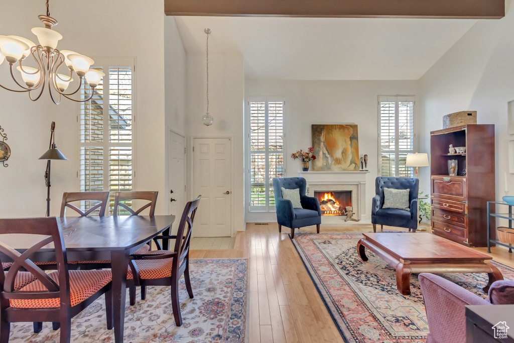 Dining space with a wealth of natural light, a notable chandelier, a lit fireplace, and light wood finished floors