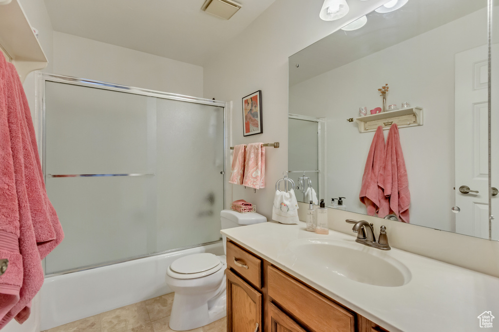 Full bath with tile patterned flooring, visible vents, toilet, vanity, and bath / shower combo with glass door