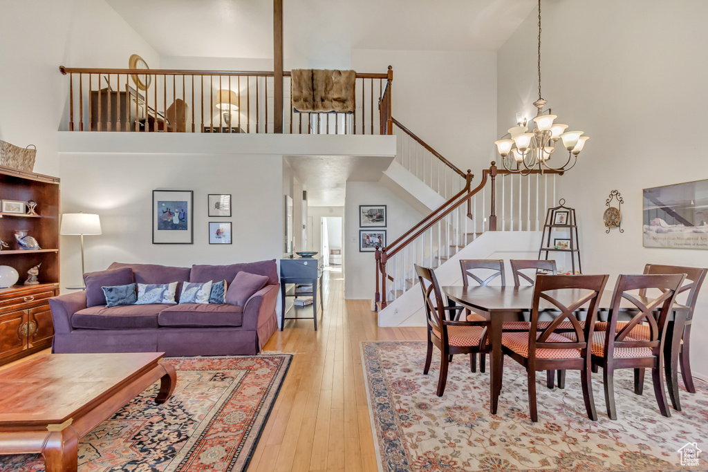 Living area featuring a chandelier, light wood-type flooring, a towering ceiling, and stairs