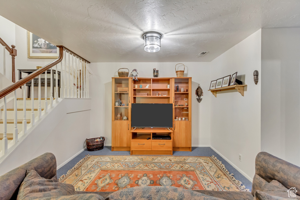 Carpeted living room featuring stairway, baseboards, and a textured ceiling
