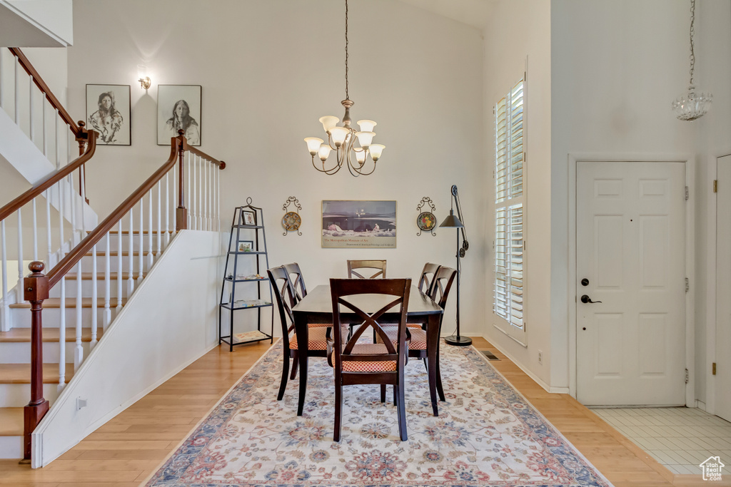 Dining space with stairs, light wood-style flooring, a towering ceiling, and a chandelier