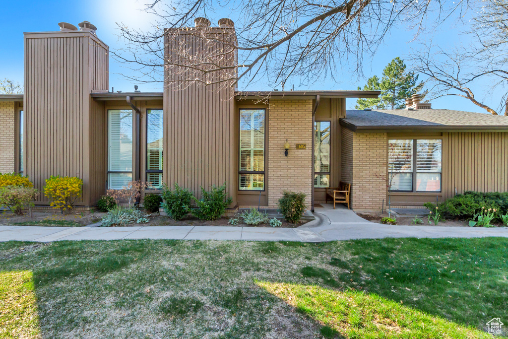 View of front of home featuring a chimney, a front lawn, and brick siding