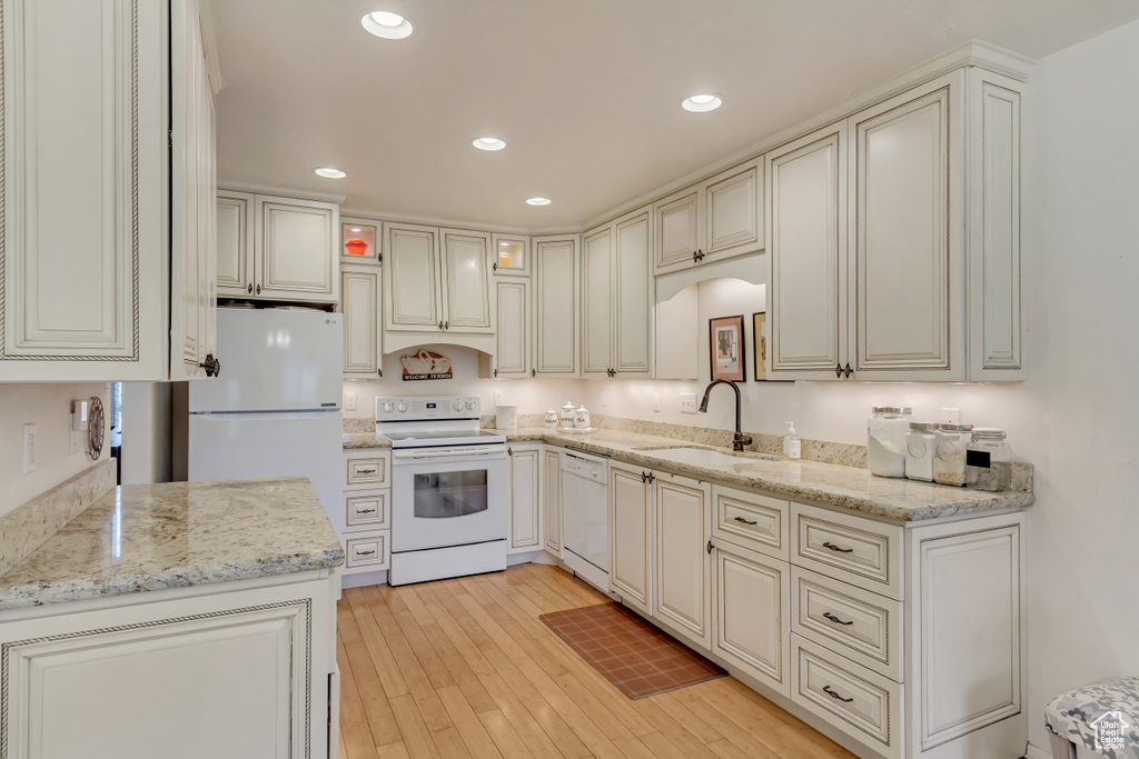Kitchen with white appliances, a sink, light wood-style floors, and light stone counters
