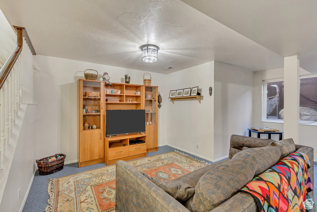 Carpeted living area featuring baseboards, a textured ceiling, and stairway