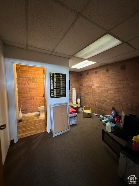 Interior space featuring a drop ceiling, carpet flooring, and brick wall