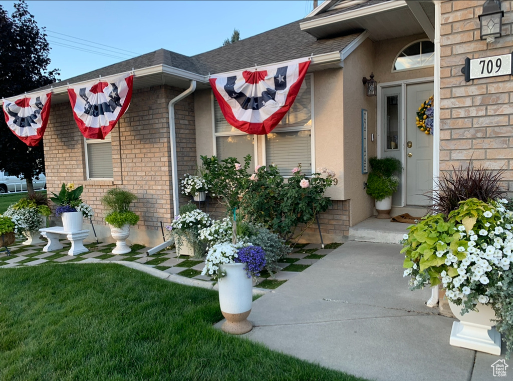 Doorway to property featuring stucco siding, brick siding, a yard, and a shingled roof
