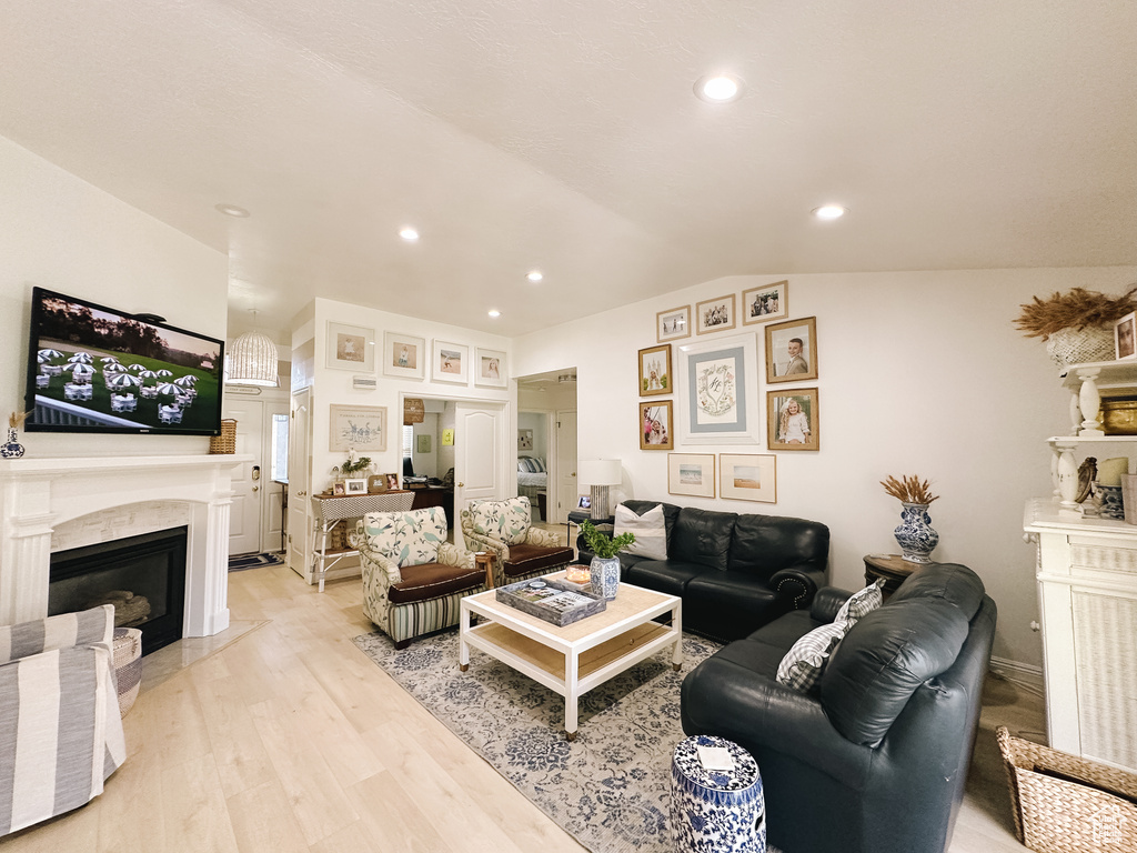 Living room with light wood-type flooring, a premium fireplace, vaulted ceiling, and recessed lighting