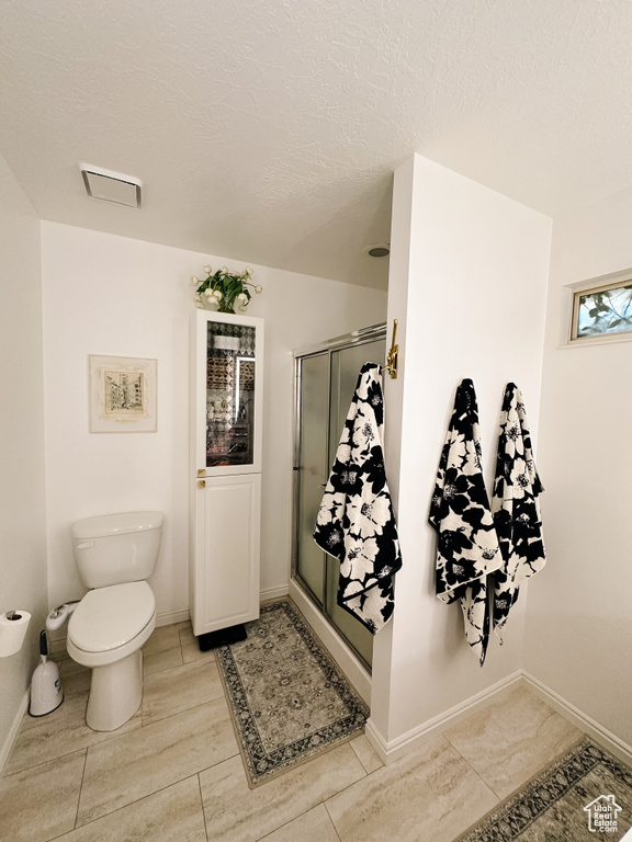 Full bath with toilet, visible vents, a textured ceiling, and a stall shower