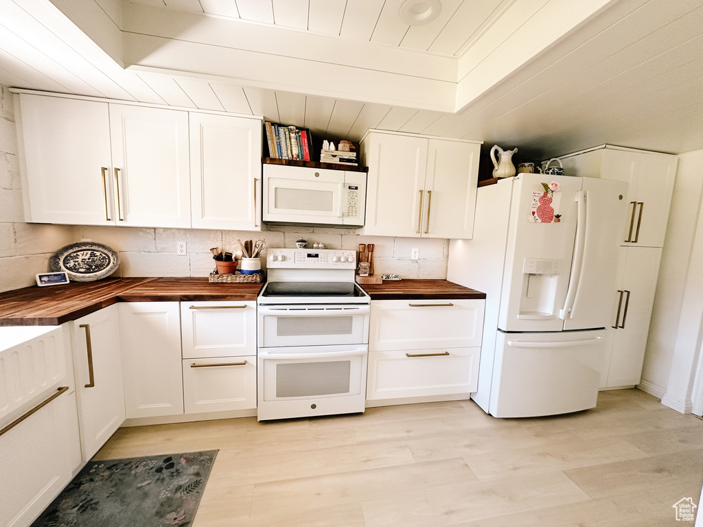 Kitchen with tasteful backsplash, wood counters, white appliances, light wood finished floors, and white cabinets
