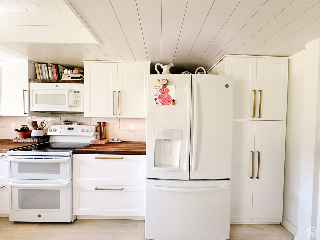 Kitchen with butcher block countertops, white cabinets, and white appliances