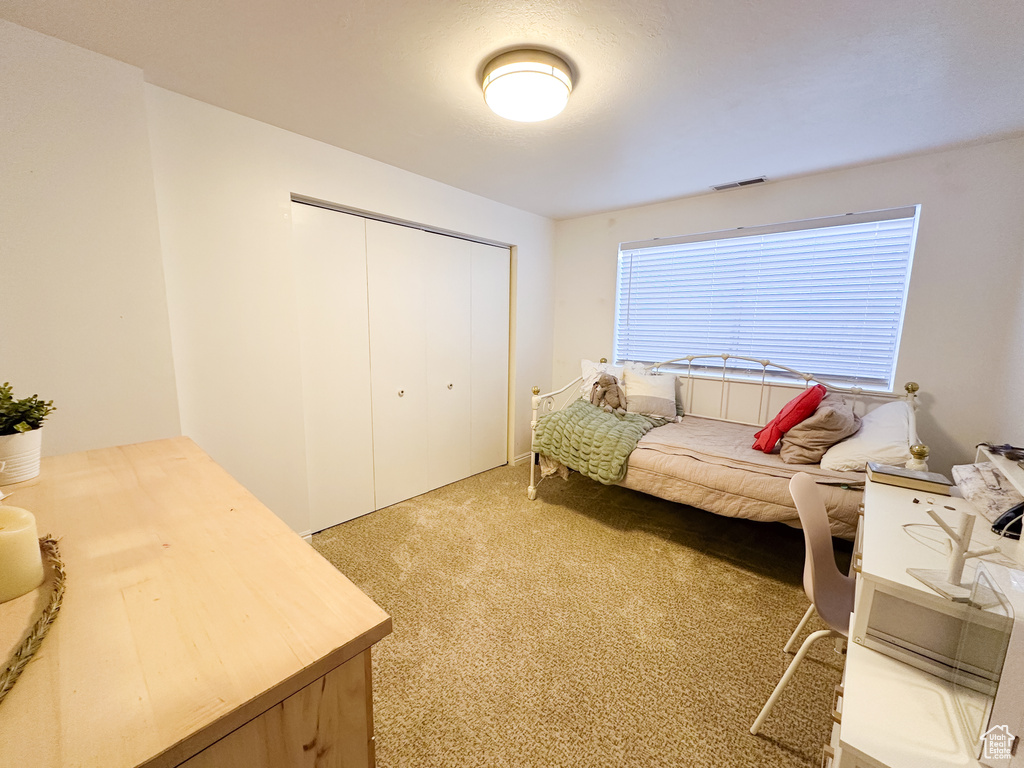 Bedroom with a closet, light colored carpet, and visible vents