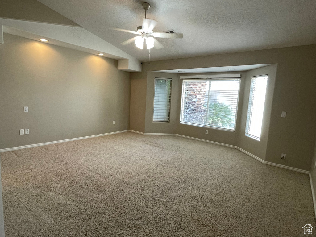 Carpeted empty room with baseboards, ceiling fan, a textured ceiling, and vaulted ceiling