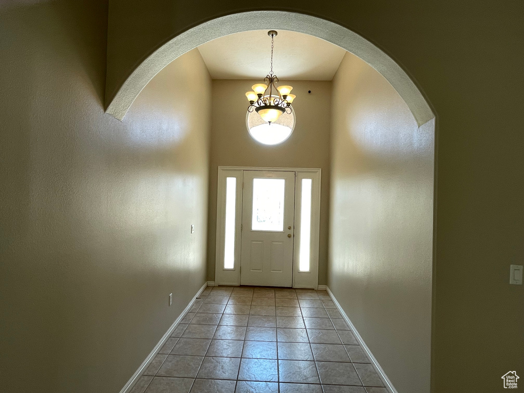 Entryway with baseboards, a notable chandelier, tile patterned flooring, and arched walkways