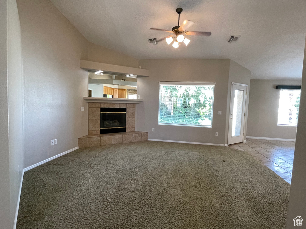 Unfurnished living room featuring a tiled fireplace, carpet, ceiling fan, baseboards, and visible vents